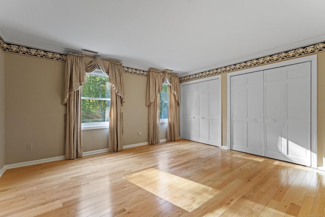 unfurnished bedroom featuring ornamental molding, light wood-type flooring, and multiple closets