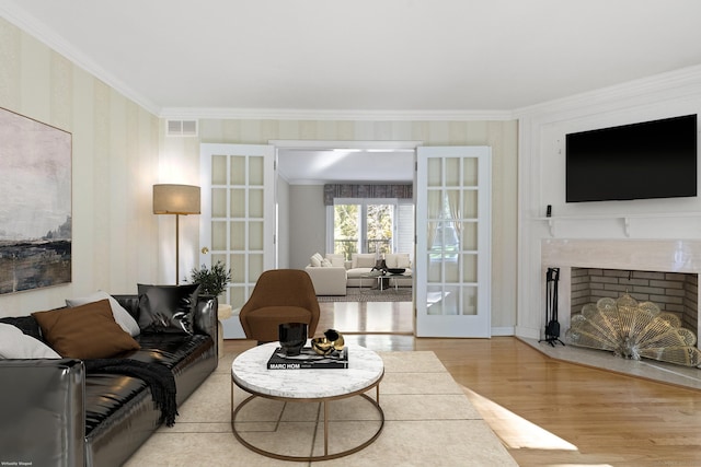 living room featuring a premium fireplace, light wood-type flooring, ornamental molding, and french doors