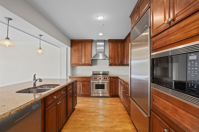 kitchen with light hardwood / wood-style flooring, built in appliances, pendant lighting, wall chimney exhaust hood, and light stone counters