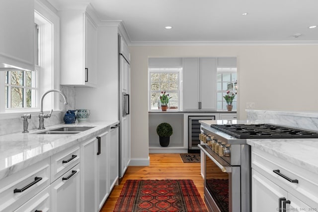 kitchen featuring light wood finished floors, light stone counters, high end range, white cabinets, and a sink