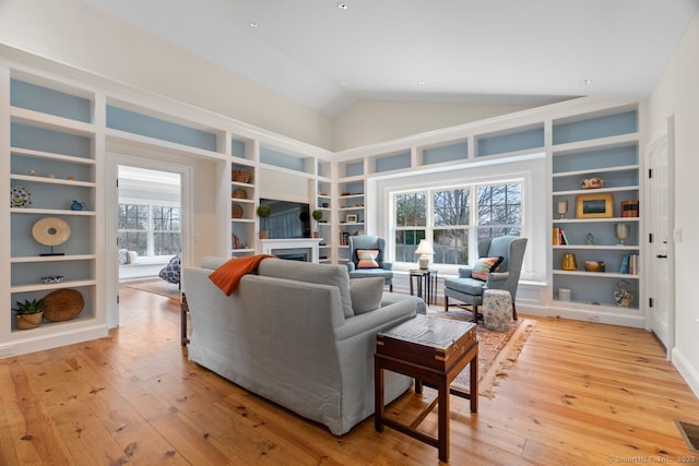 living room featuring high vaulted ceiling, built in features, recessed lighting, light wood-style floors, and a fireplace