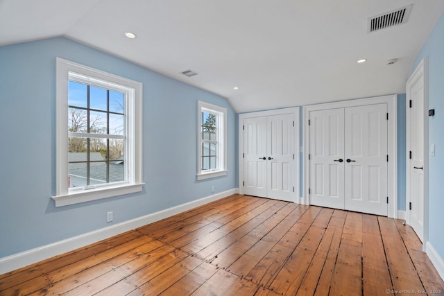 unfurnished bedroom with vaulted ceiling, visible vents, two closets, and wood-type flooring