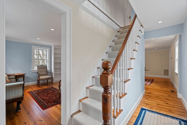 stairway featuring visible vents, crown molding, baseboards, and wood finished floors