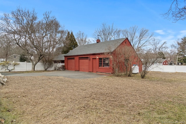 view of outdoor structure with a garage, driveway, and fence