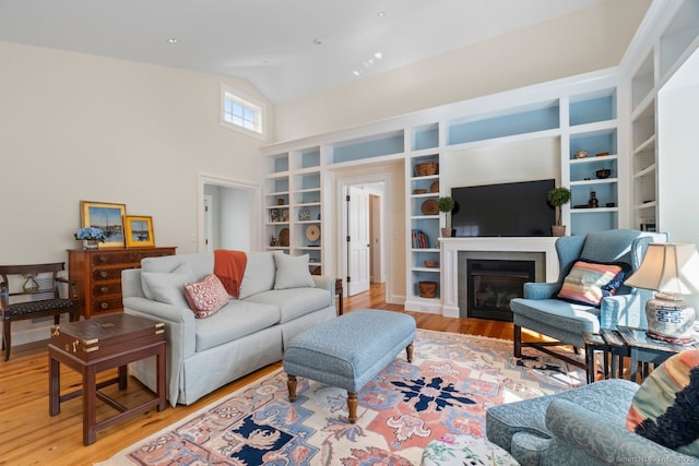 living area with a glass covered fireplace, wood finished floors, and high vaulted ceiling