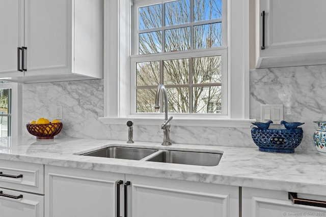 kitchen featuring a sink, decorative backsplash, light stone counters, and white cabinets