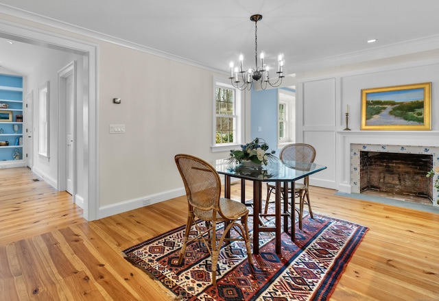 dining room featuring light wood finished floors, a notable chandelier, a fireplace, and crown molding