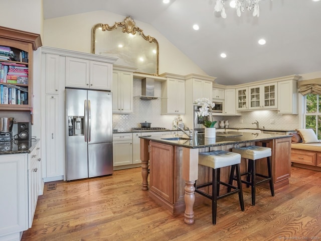 201 Shore Rd, Greenwich, CT 06830 - kitchen featuring wall chimney range hood, a kitchen island with sink, light wood-style flooring, stainless steel appliances, and decorative backsplash