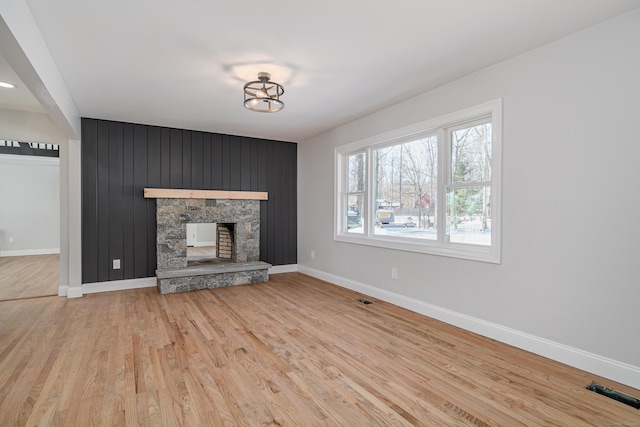 unfurnished living room featuring a stone fireplace and light wood-type flooring