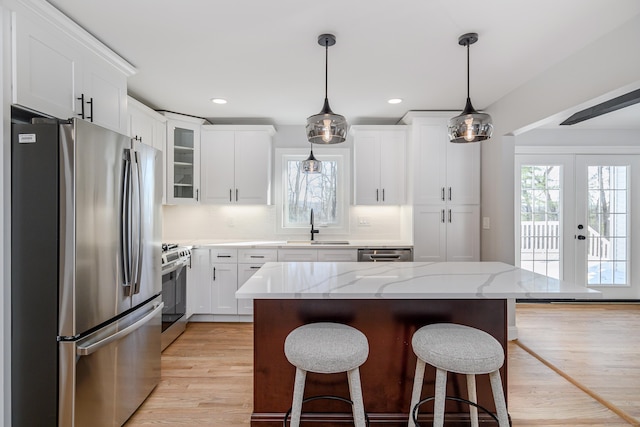 kitchen featuring appliances with stainless steel finishes, light stone counters, sink, decorative light fixtures, and a center island