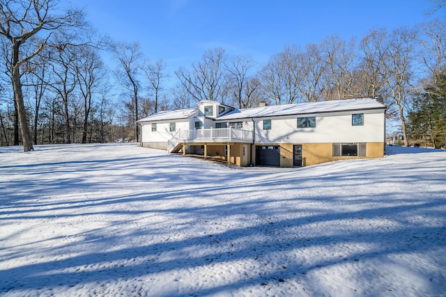 snow covered rear of property with a garage and a deck