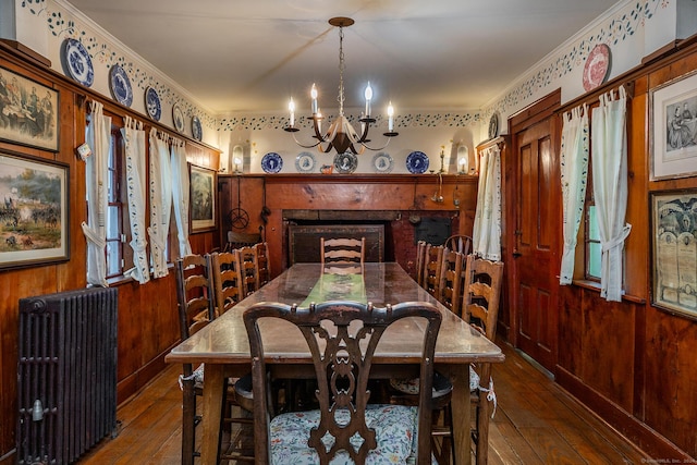 dining area with radiator, wood-type flooring, wooden walls, and ornamental molding