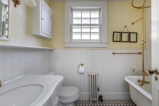 full bath with radiator, a wainscoted wall, a soaking tub, and toilet