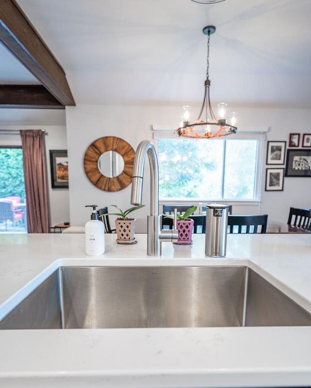 kitchen featuring sink, beam ceiling, an inviting chandelier, and pendant lighting