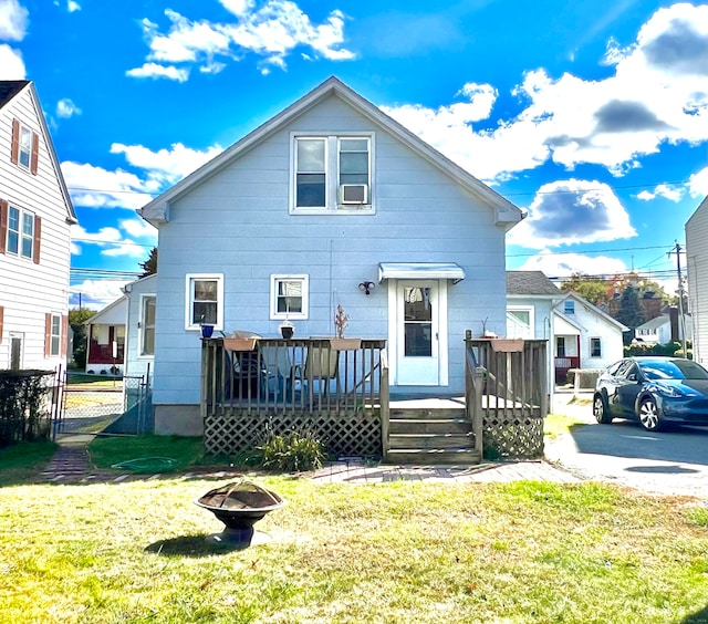 rear view of property featuring a fire pit, a wooden deck, and a lawn