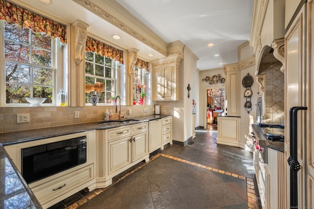 kitchen with tasteful backsplash, ornamental molding, black microwave, sink, and cream cabinetry