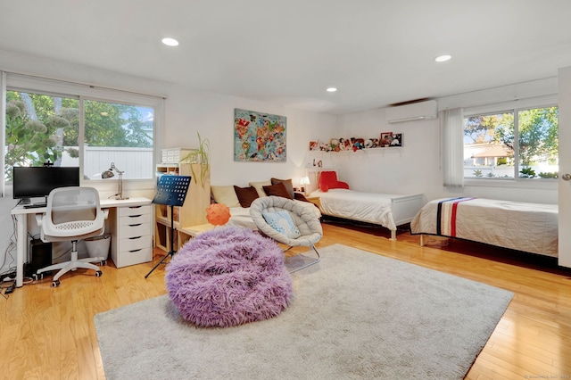 bedroom with an AC wall unit, multiple windows, and light hardwood / wood-style flooring