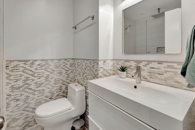 bathroom with toilet, vanity, a tile shower, and tile walls