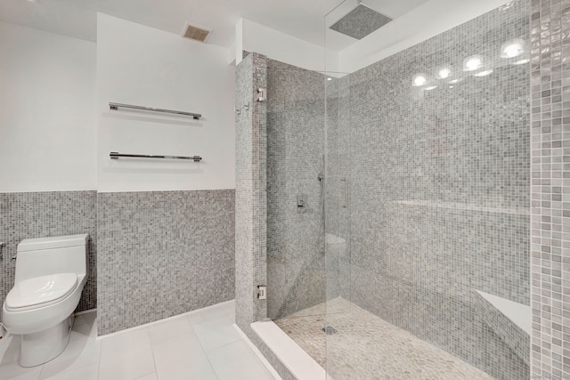 bathroom with tile walls, a tile shower, toilet, and tile patterned flooring