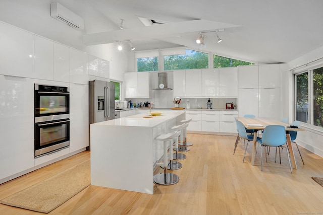 kitchen featuring white cabinets, track lighting, appliances with stainless steel finishes, extractor fan, and light wood-type flooring