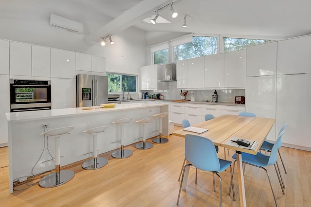 kitchen featuring light hardwood / wood-style floors, a wall unit AC, stainless steel appliances, white cabinetry, and high vaulted ceiling