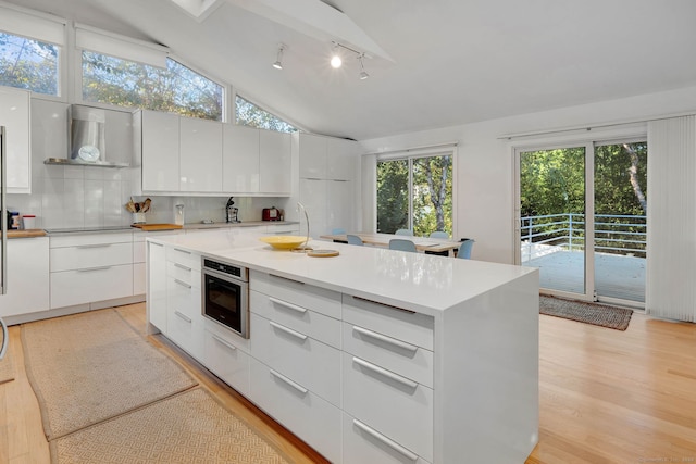 kitchen with oven, light wood-type flooring, white cabinetry, wall chimney exhaust hood, and a center island with sink