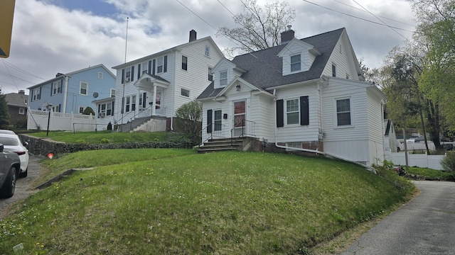 view of front facade featuring a shingled roof, fence, a front yard, and a chimney