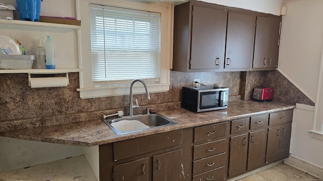 kitchen featuring a sink, stainless steel microwave, backsplash, and dark brown cabinetry