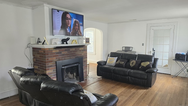 living area featuring crown molding, arched walkways, a brick fireplace, and wood finished floors