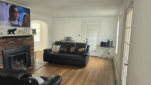 living room featuring a brick fireplace, arched walkways, baseboard heating, and wood finished floors