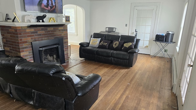 living room featuring arched walkways, a fireplace, a baseboard radiator, and hardwood / wood-style flooring