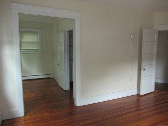 corridor with a baseboard heating unit and dark wood-type flooring