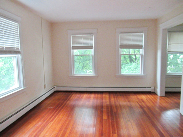 spare room featuring dark hardwood / wood-style flooring, a healthy amount of sunlight, and a baseboard heating unit