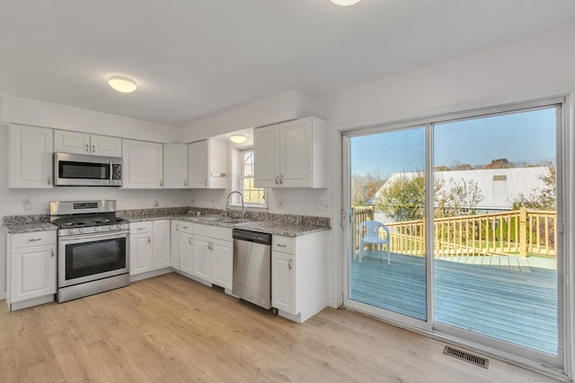 kitchen with white cabinetry, sink, stainless steel appliances, and light hardwood / wood-style flooring