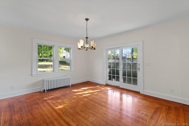 spare room featuring an inviting chandelier, hardwood / wood-style flooring, a healthy amount of sunlight, and radiator