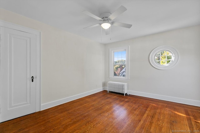 spare room with dark wood-type flooring, radiator, and ceiling fan