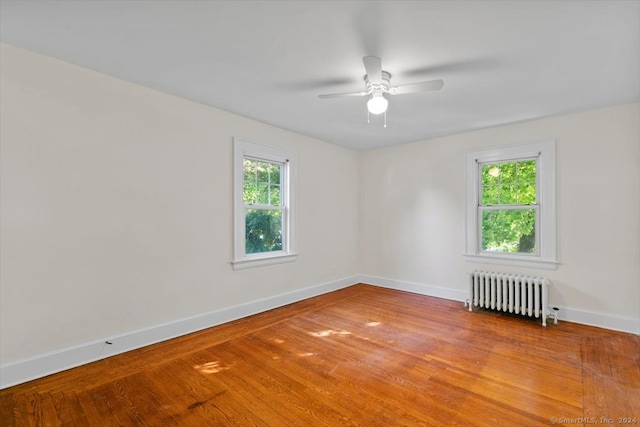 empty room featuring ceiling fan, hardwood / wood-style flooring, and radiator heating unit