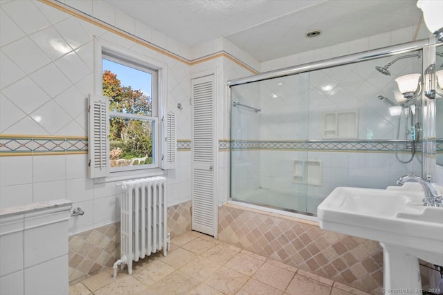 bathroom featuring radiator heating unit, combined bath / shower with glass door, tile walls, sink, and tile patterned floors