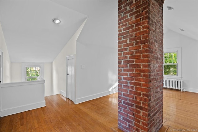 hallway with vaulted ceiling, radiator heating unit, and wood-type flooring