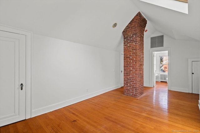 bonus room featuring lofted ceiling with skylight, ornate columns, radiator heating unit, and light hardwood / wood-style floors