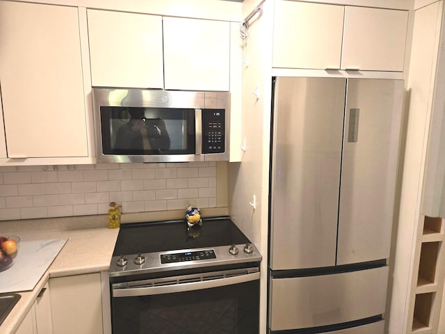 kitchen with tasteful backsplash, white cabinets, and appliances with stainless steel finishes