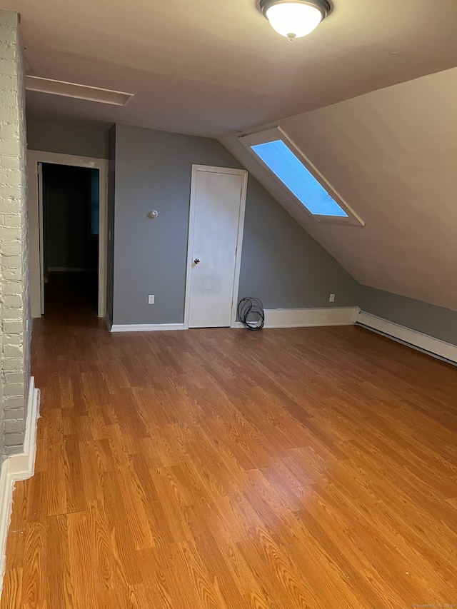 additional living space featuring vaulted ceiling with skylight and light wood-type flooring