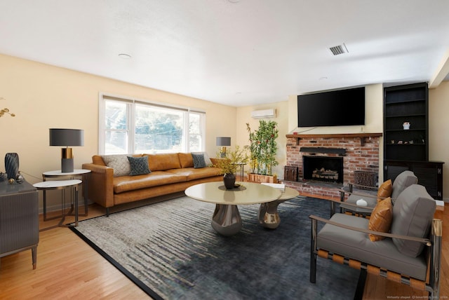 living room featuring a wall mounted AC, a fireplace, and light wood-type flooring