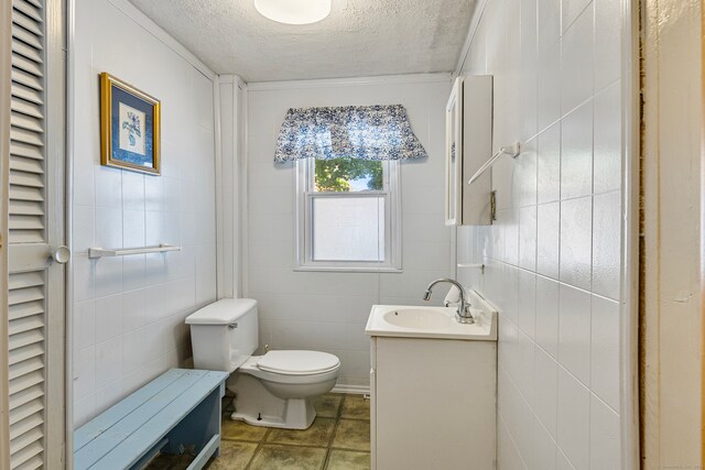 bathroom with vanity, toilet, a textured ceiling, and tile walls