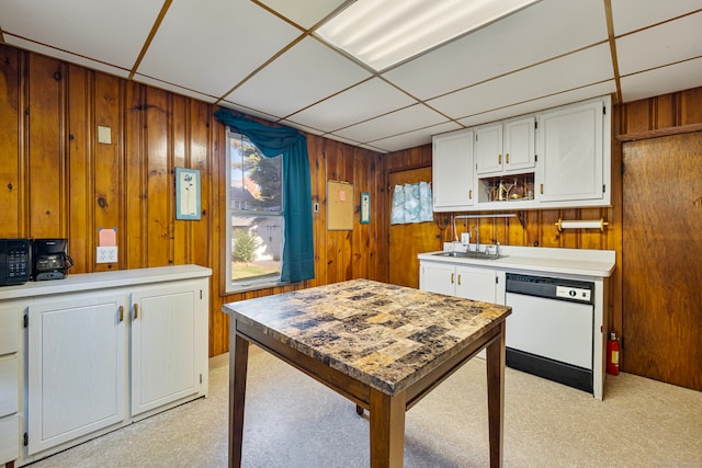 kitchen with dishwasher, white cabinets, a paneled ceiling, and wood walls