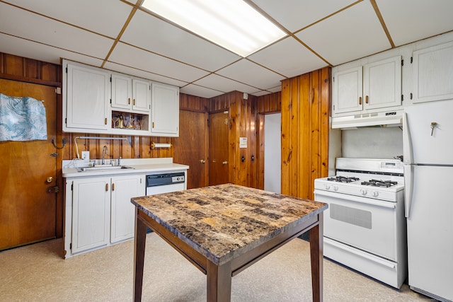 kitchen with white appliances, sink, white cabinetry, a paneled ceiling, and wooden walls