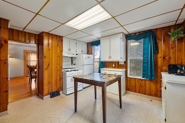 kitchen with white cabinets, a paneled ceiling, white appliances, and wood walls