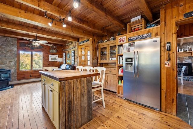 kitchen with stainless steel fridge, light hardwood / wood-style floors, a wood stove, and beam ceiling