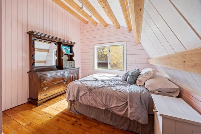 bedroom featuring wood walls, beamed ceiling, and light wood-type flooring