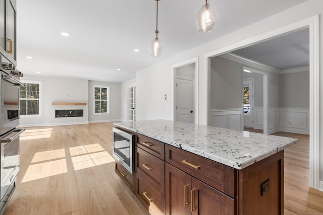 kitchen featuring a kitchen island, stainless steel appliances, crown molding, decorative light fixtures, and light wood-type flooring